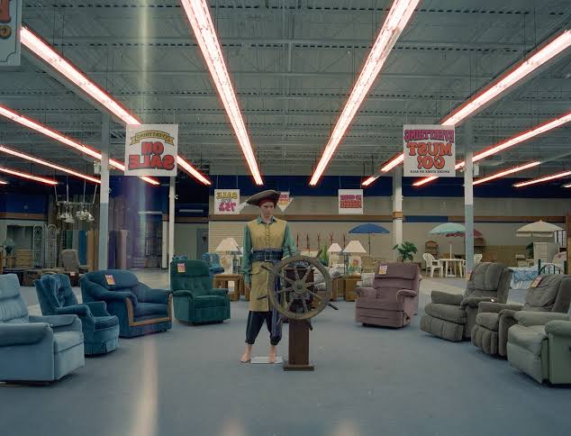 The store showroom with a ship's wheel on a pedestal, ranked recliners, and magenta chevron fluorescent tubes overhead.